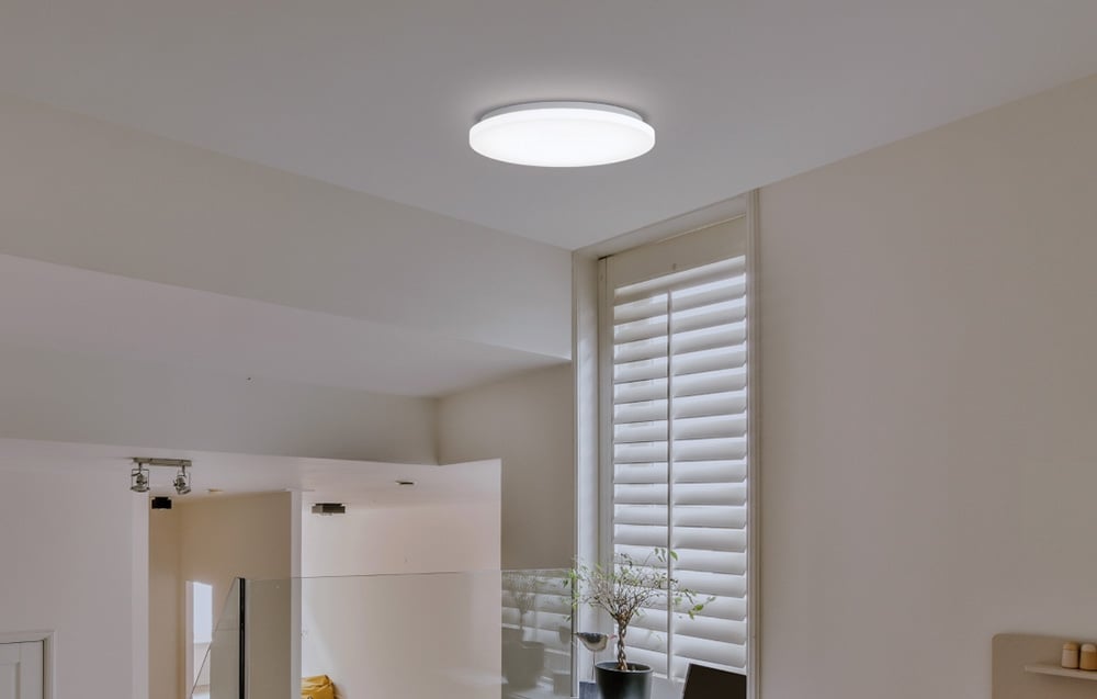 Lampa Yeelight MercuryE C300 namontovaná v interiéri s vertikálnymi žalúziami a kvetináčom na parapete.