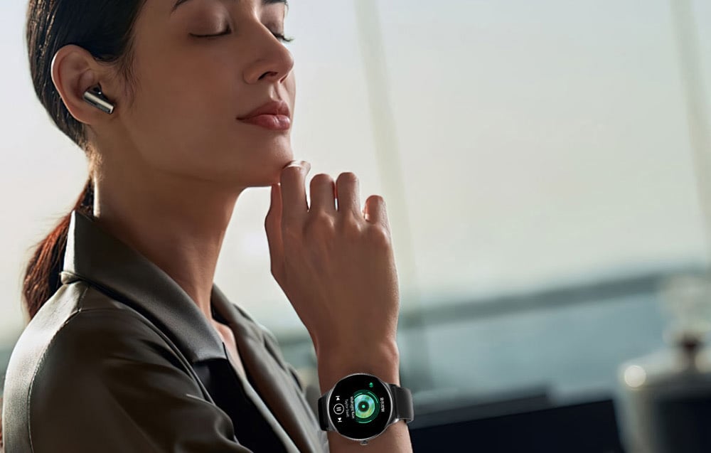 Žena so zopnutými vlasmi a so slúchadlom v uchu. Na zápästí smart hodinky so zapnutým prehrávačom hudby.