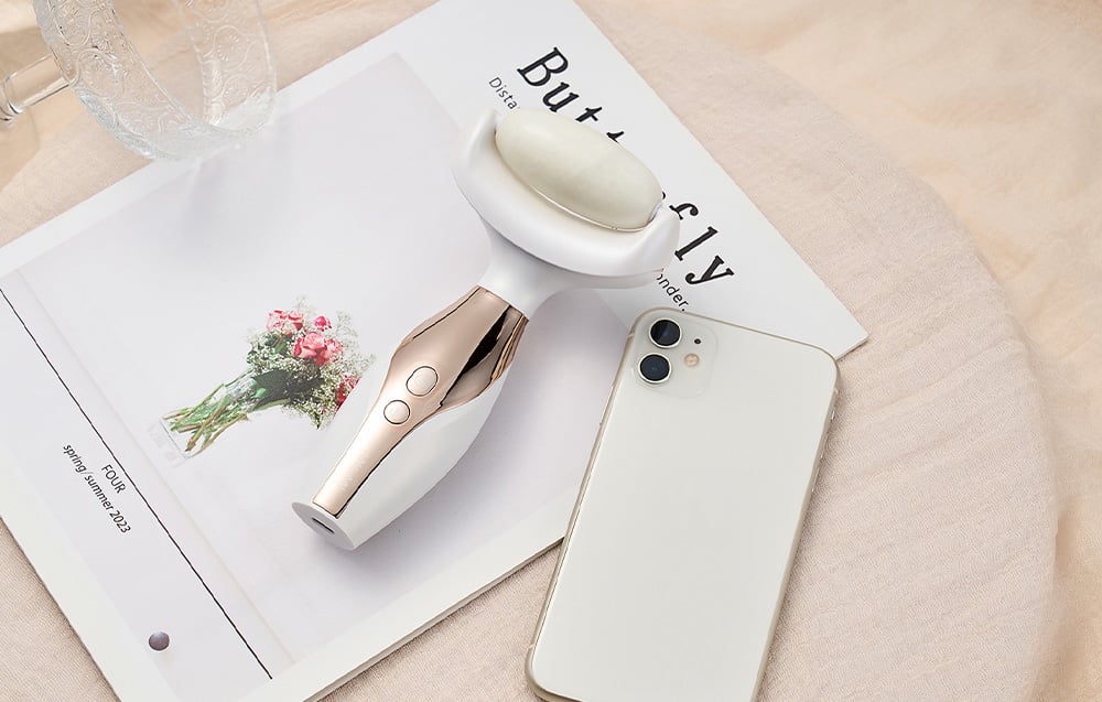 Elektrický masážny prístroj na stole vedľa novín a smartfónu