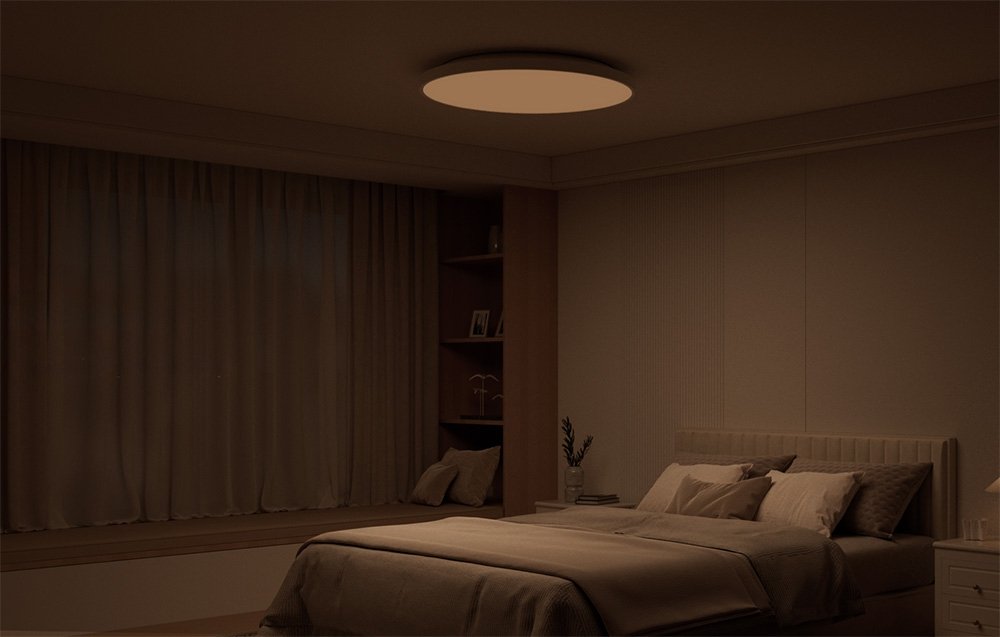 Zatemnený interiér spálne s posteľou a stropným svietidlom Yeelight Mercury C300 žiariacim teplým svetlom.