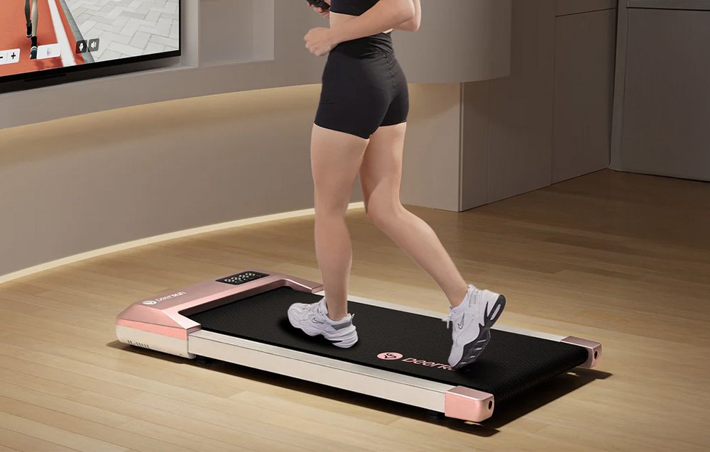 Žena bežiaca na ružovo-bielom bežeckom páse DeerRun, pozerajúca sa na obrazovku so simuláciou behu