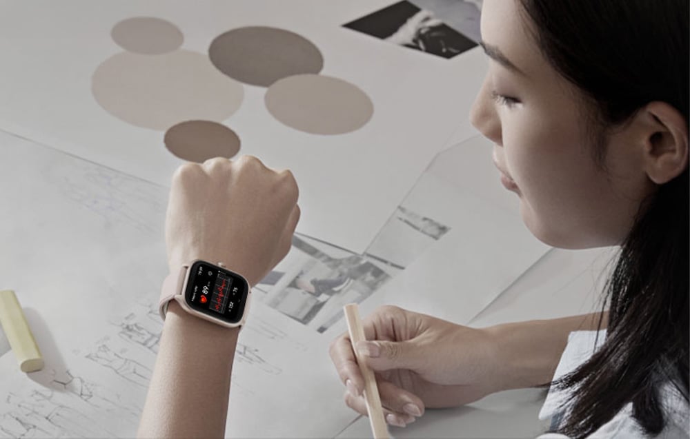 Žena pracujúca za stolom sa pozerá na inteligentné hodinky na svojom zápästí