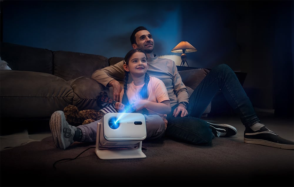 Muž a dievča sedia na podlahe v obývacej izbe a pozerajú film z malého projektora umiestneného pred nimi.