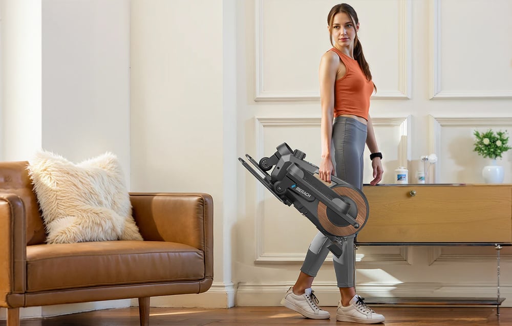 Žena nesie zložený mini eliptický trenažér Merach, čím demonštruje jeho kompaktný dizajn.