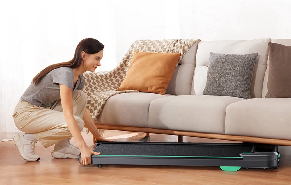 Žena v sivej košeli posúva bežecký pás pod pohovku.