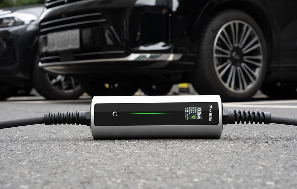 Nabíjačka elektromobilov ležiaca na zemi, zaparkované autá v pozadí