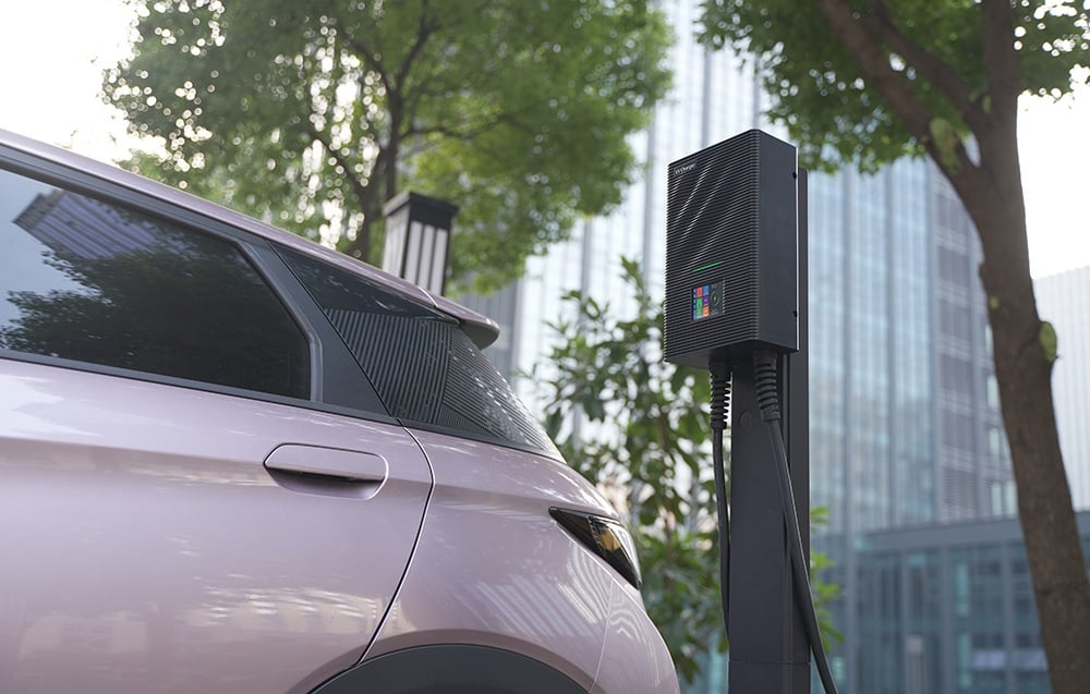 Svetlé auto pripojené k nabíjačke EV, s budovami v pozadí