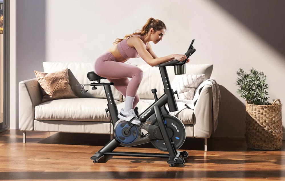 Žena intenzívne cvičí na stacionárnom bicykli v obývacej izbe