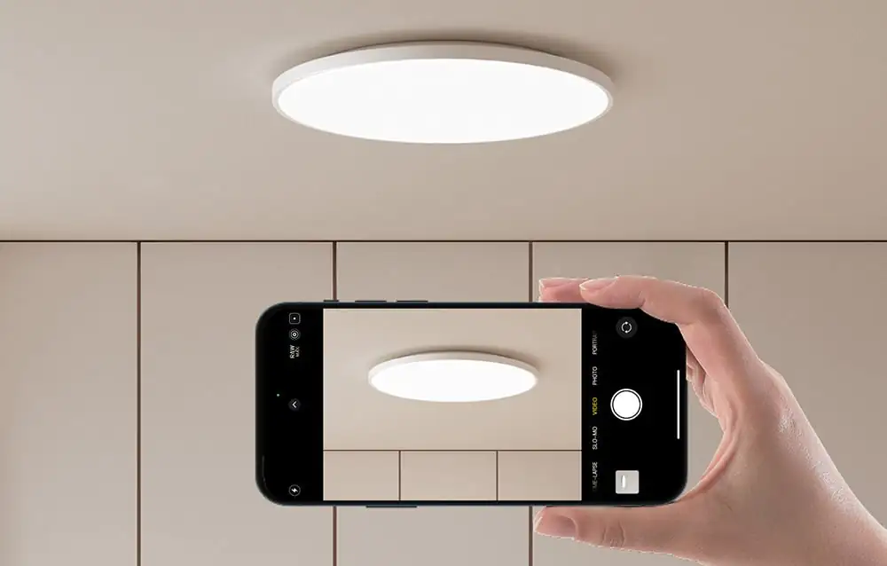 Ruka držiaca smartfón s fotoaparátom namiereným na zapnuté stropné svietidlo Yeelight.